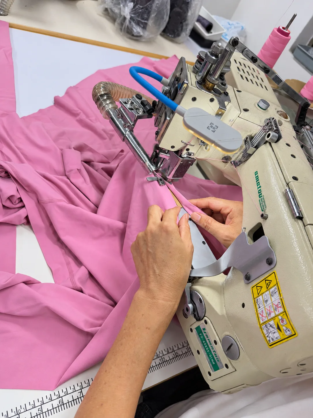Hands guiding pink garment fabric through an industrial sewing machine